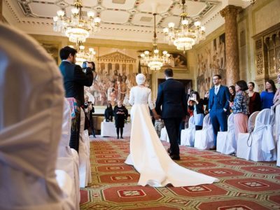 Couple walking down wedding aisle in grand room with big chandeliers